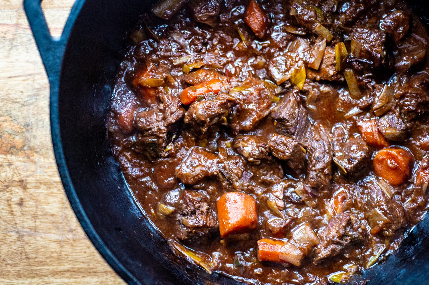 A Dutch oven filled with beef stew, showing tender beef chunks, carrots, potatoes, and a glossy, richly browned broth bubbling gently on the stove