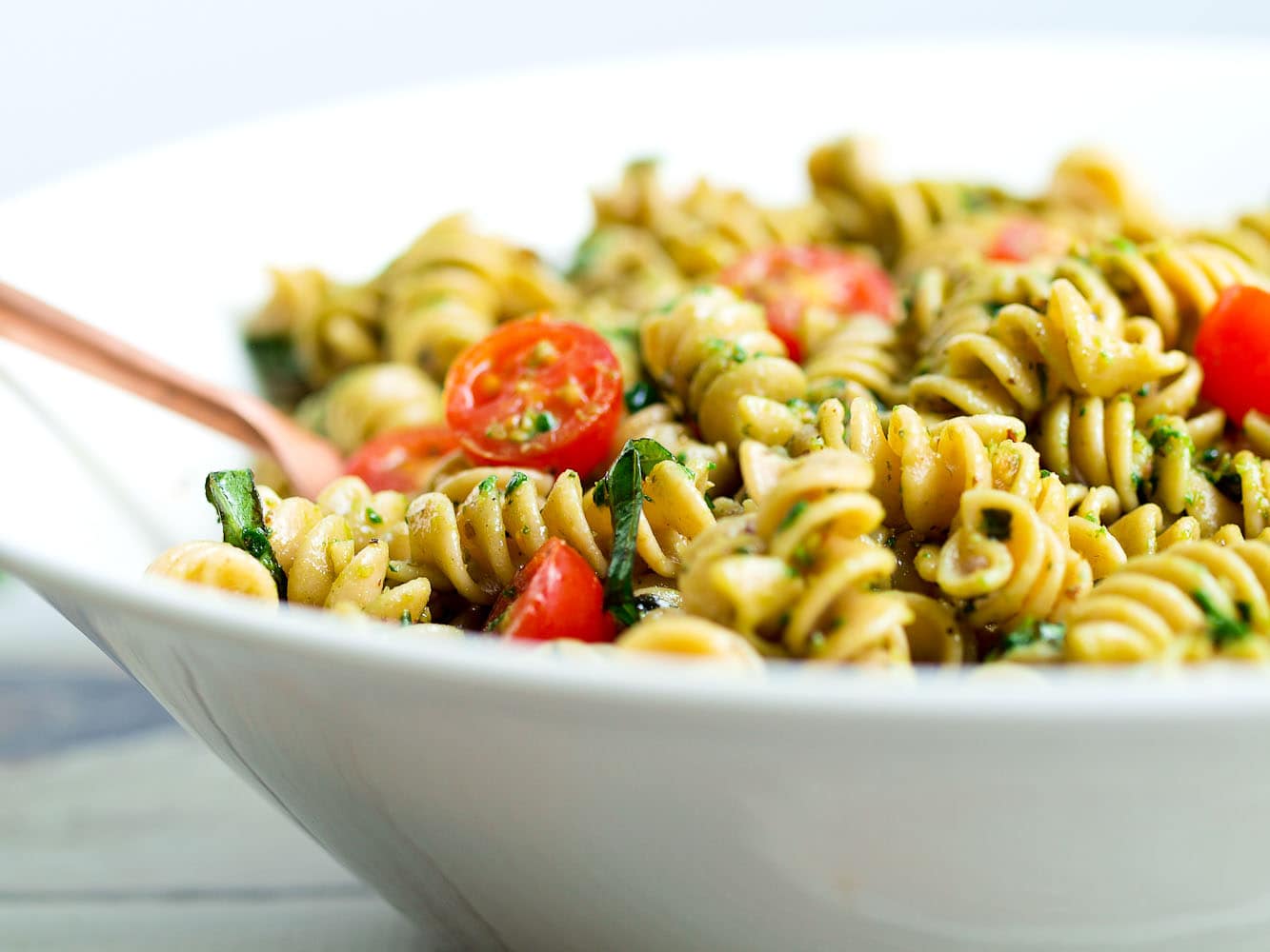 A bowl of pasta tossed with glossy basil pesto, topped with grated Parmesan and toasted pine nuts on a simple weeknight table