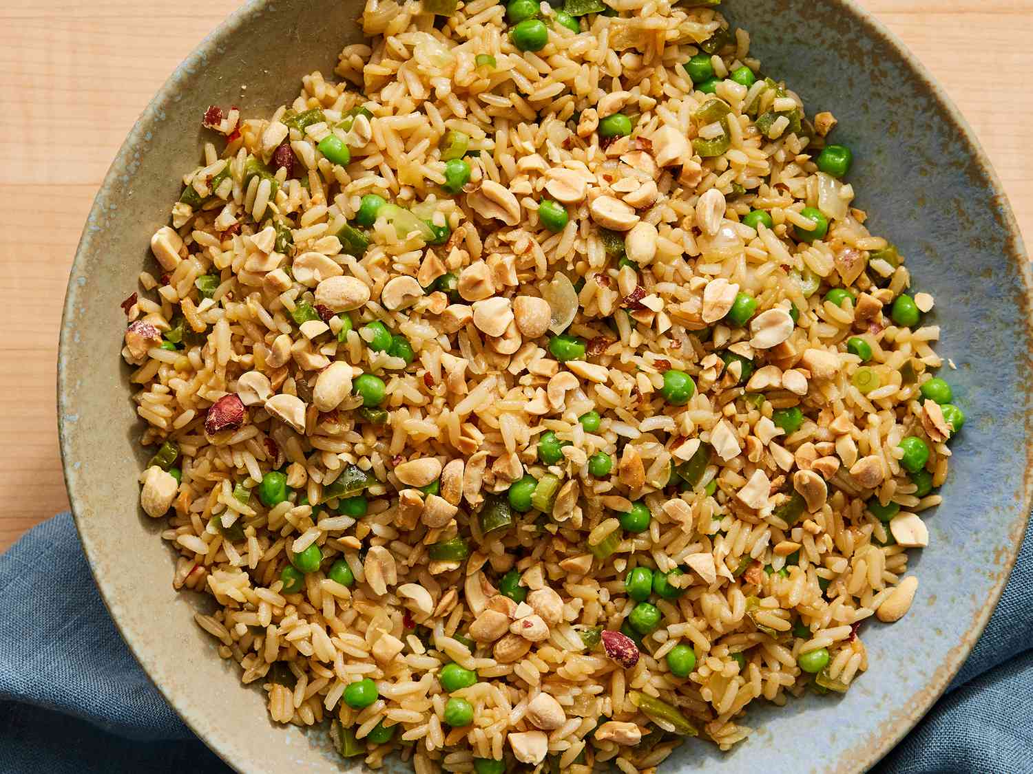 A bowl of vegetable fried rice with peas, carrots, scallions, and fluffy separated grains of rice, photographed on a casual kitchen table