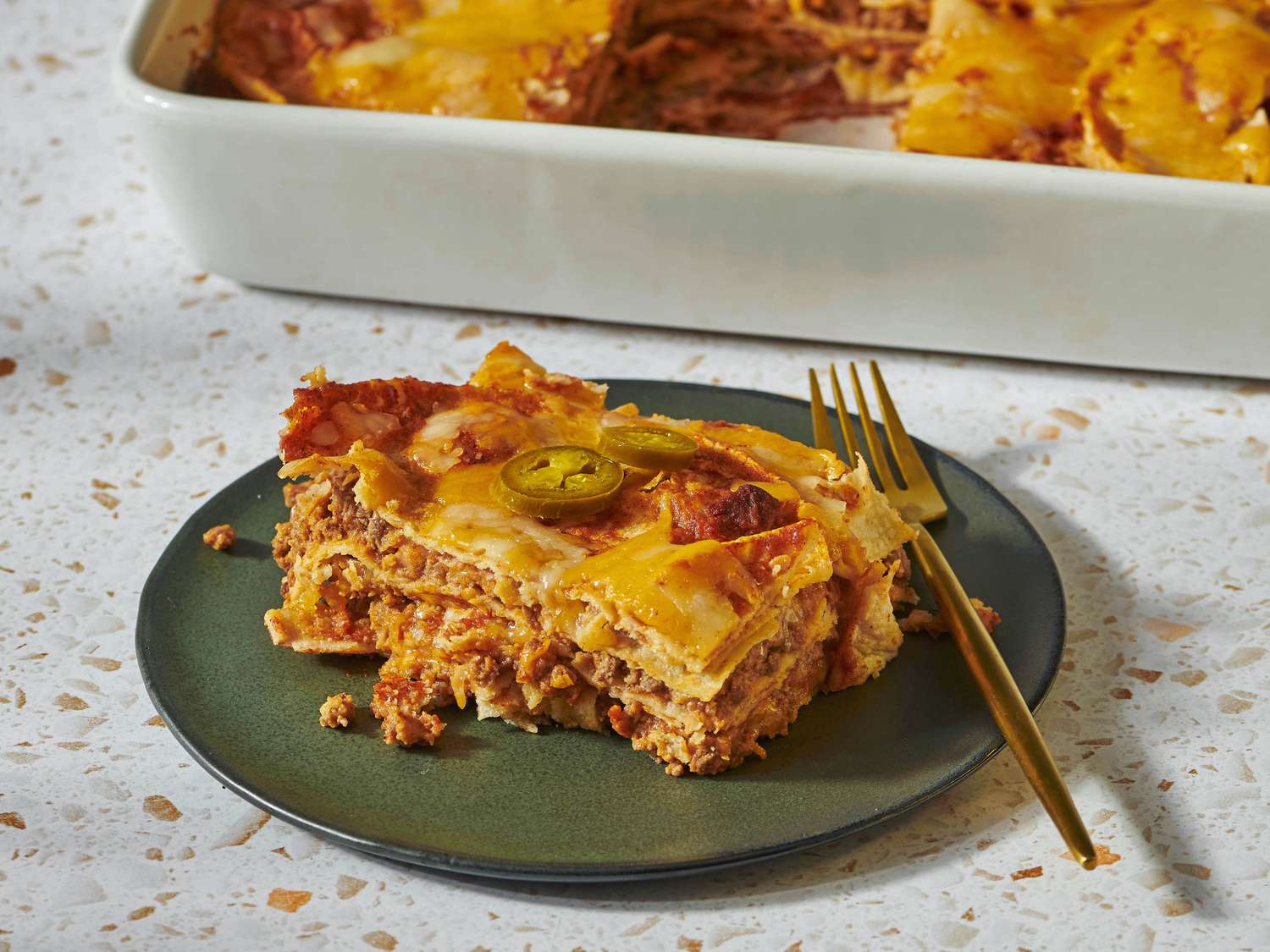 A bubbling baking dish of red-sauced enchiladas with melted cheese being pulled from the oven using oven mitts
