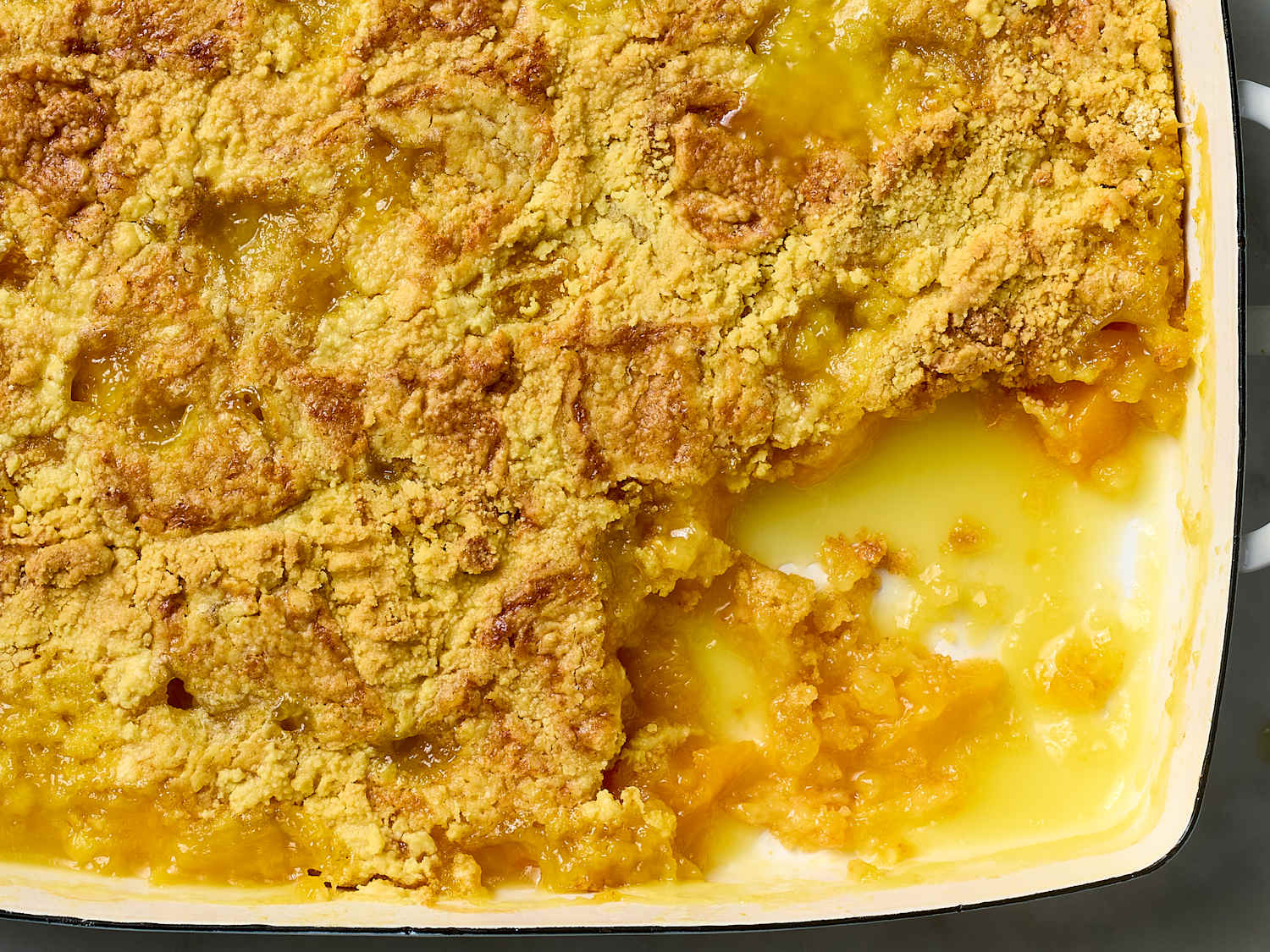 A bubbling peach cobbler with a golden, craggy cake mix topping cooling in a rustic baking dish on a kitchen counter