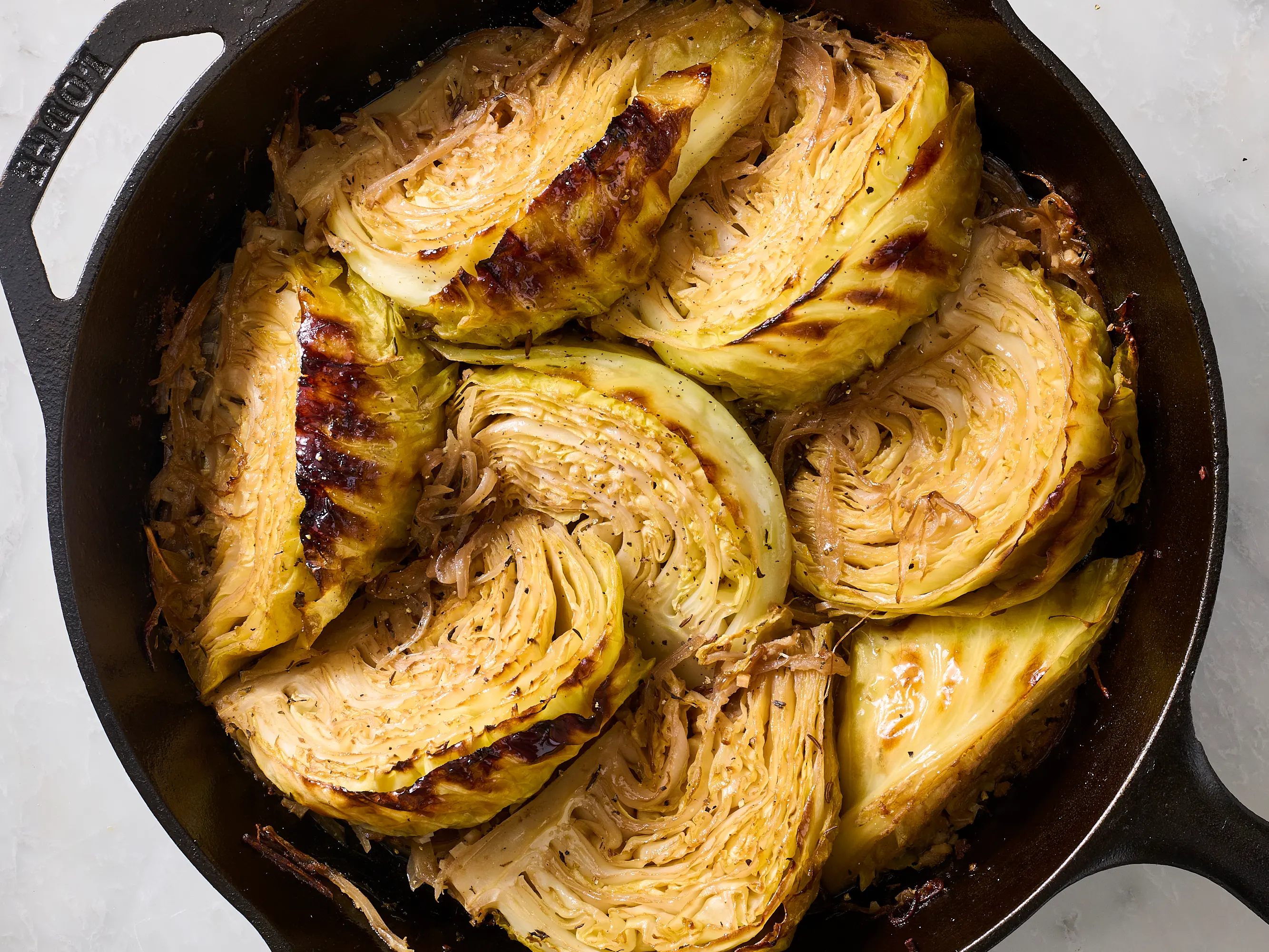 A cast iron skillet filled with deeply browned, tender cabbage wedges with caramelized edges and glossy butter pooling lightly at the bottom