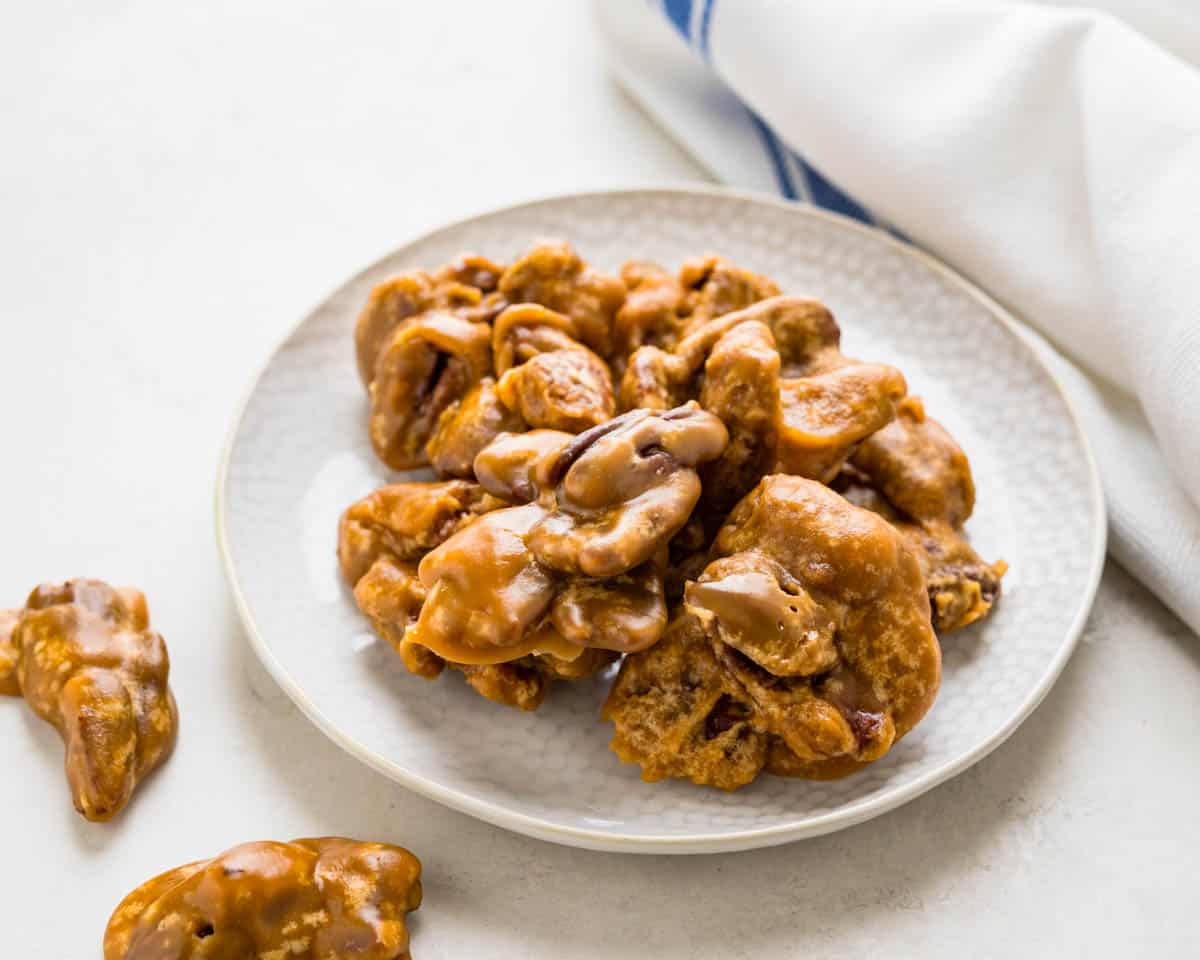 A ceramic bowl filled with glossy, caramel-coated praline pecans on a wooden kitchen counter with soft natural light
