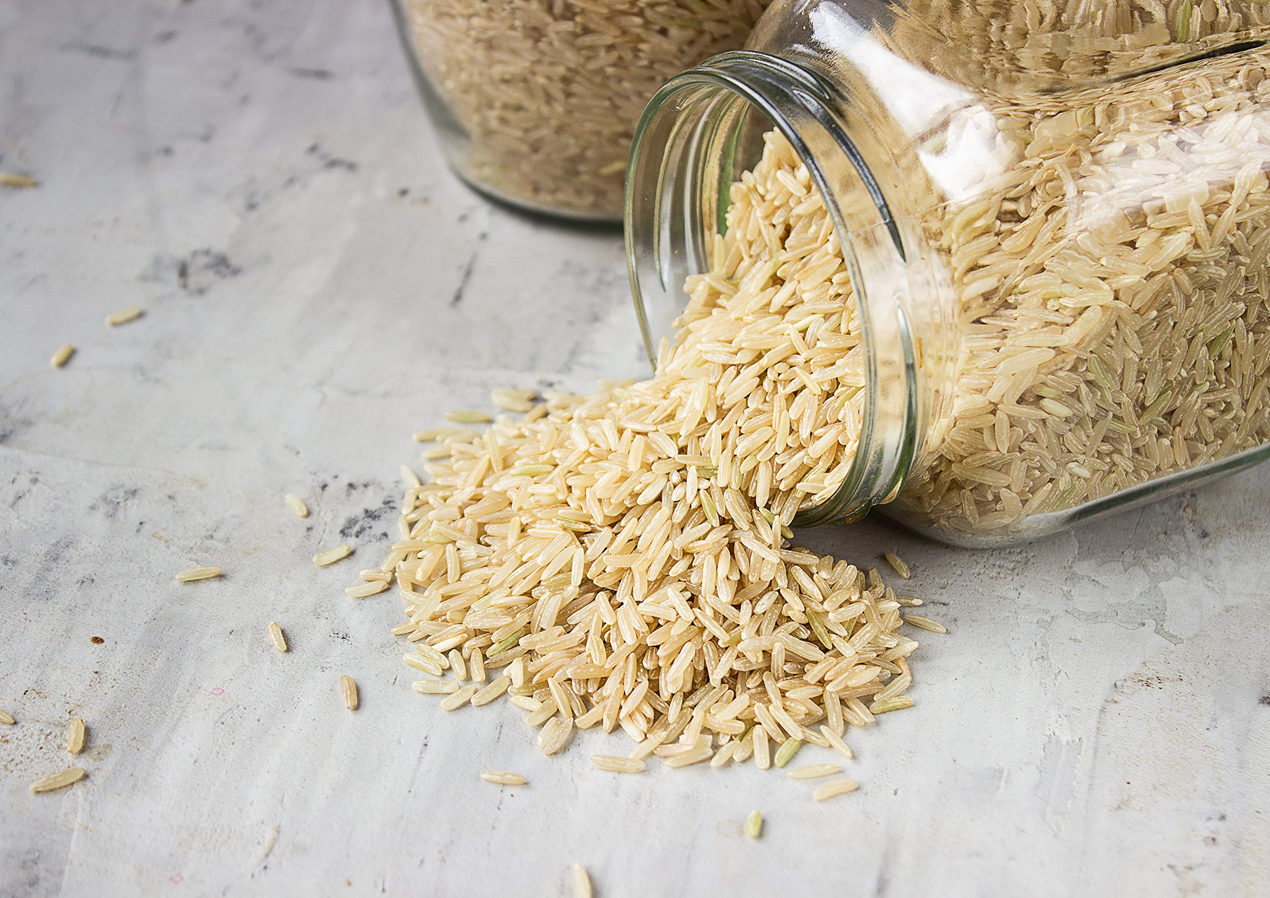A ceramic bowl filled with uncooked long-grain brown rice on a wooden kitchen counter with soft window light