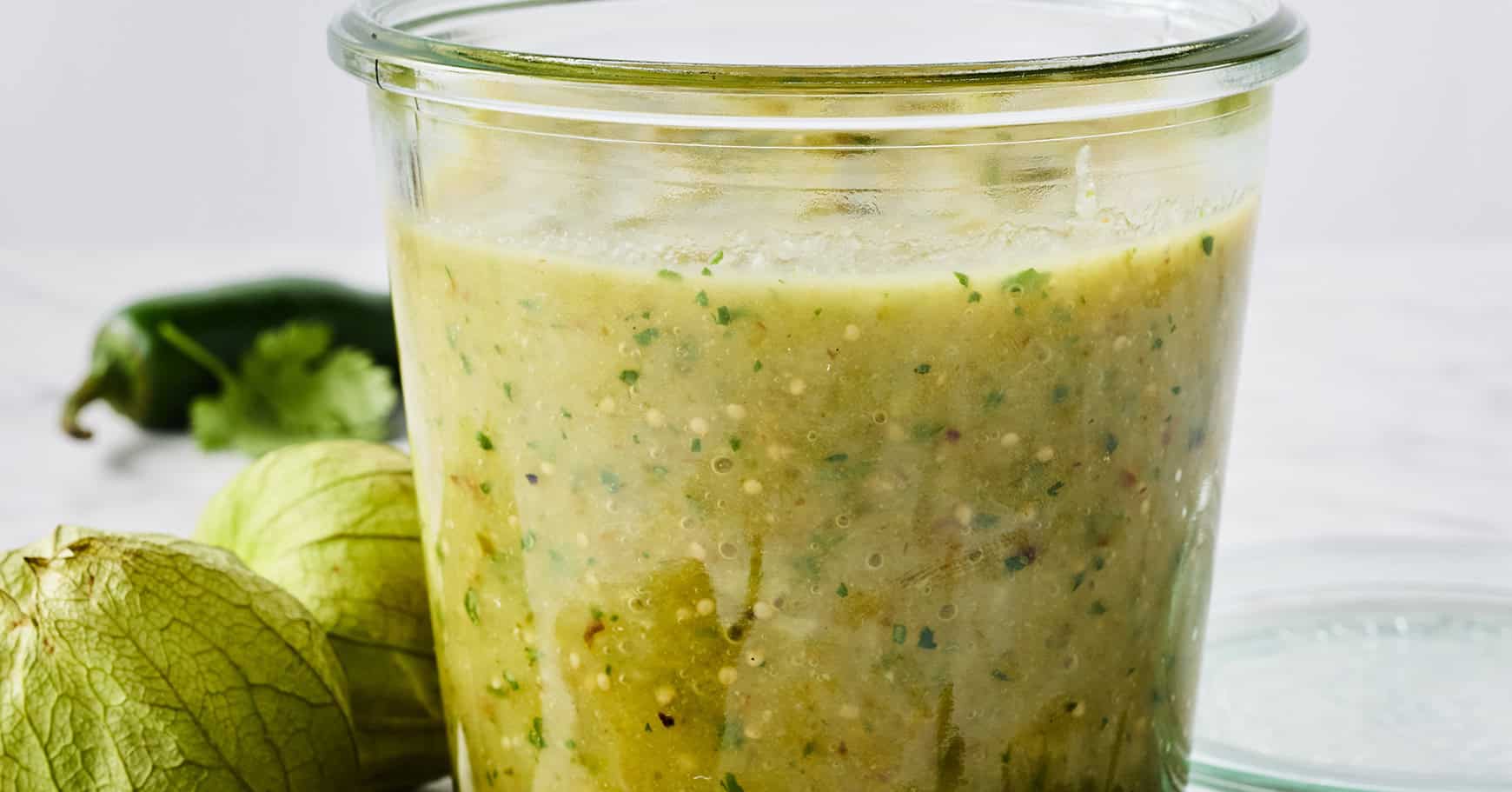 A cook tasting green enchilada sauce from a spoon over a pot on the stove
