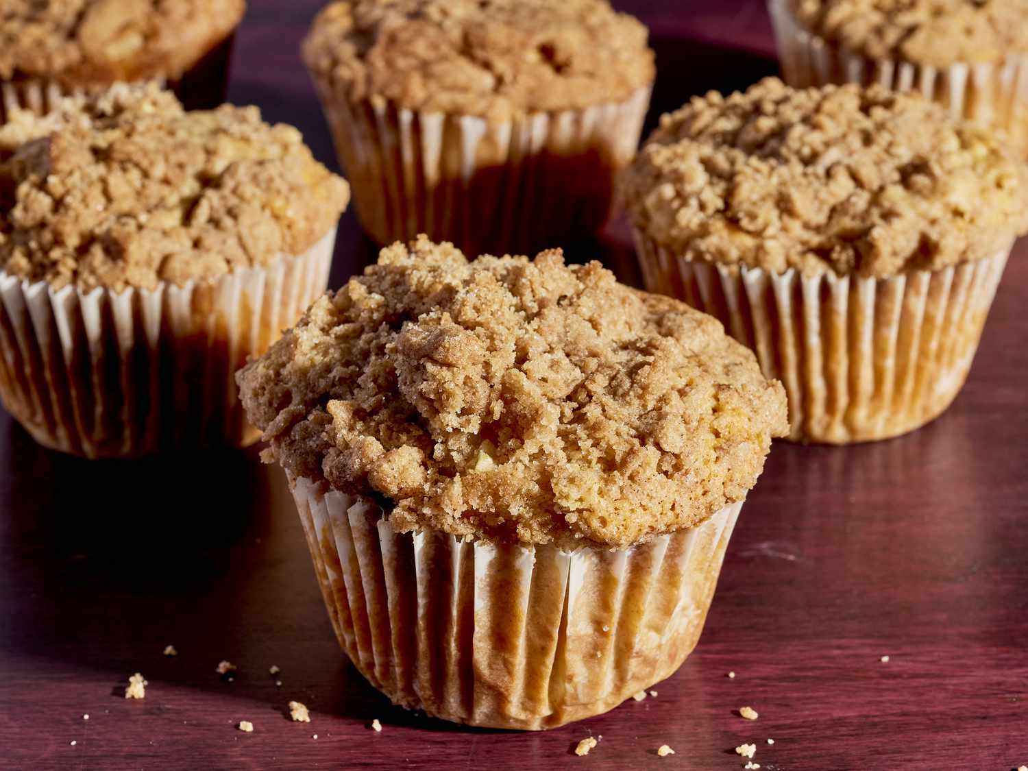 A dozen cinnamon apple muffins with golden crumb topping cooling on a wire rack on a light kitchen counter