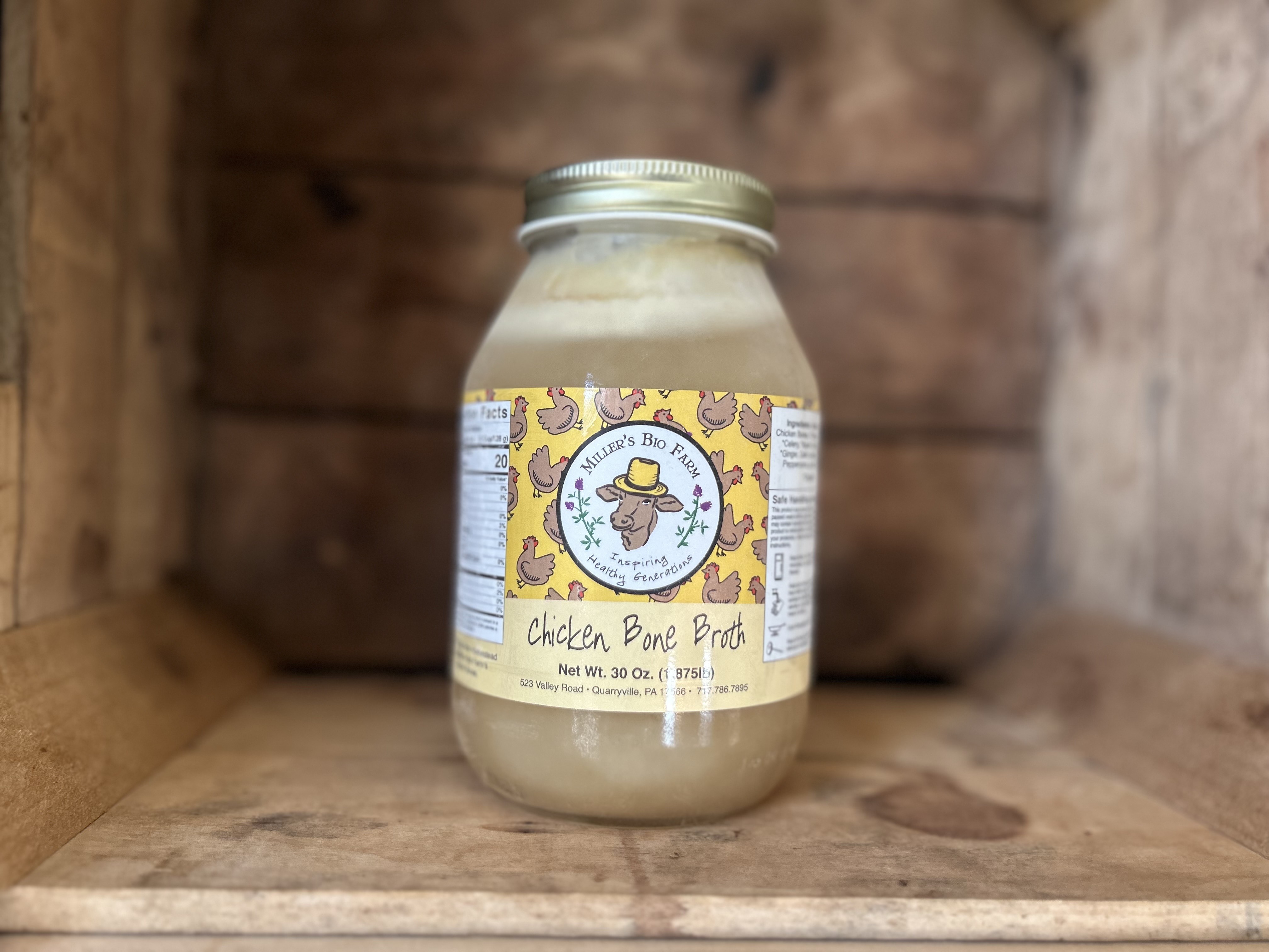 A glass jar filled with golden chicken bone broth on a kitchen counter with a few peppercorns and thyme sprigs nearby