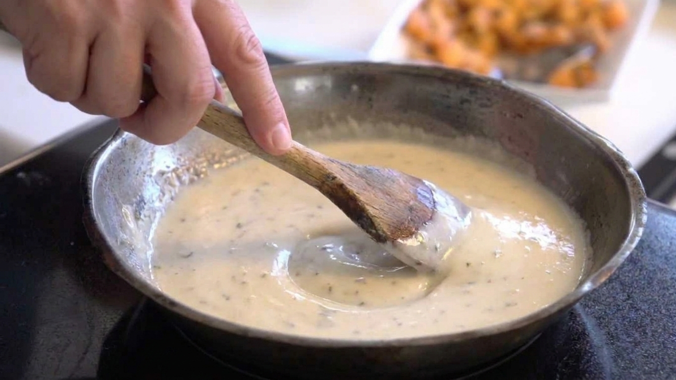A hand stirring a smooth, glossy cheese sauce with a wooden spoon in a small saucepan