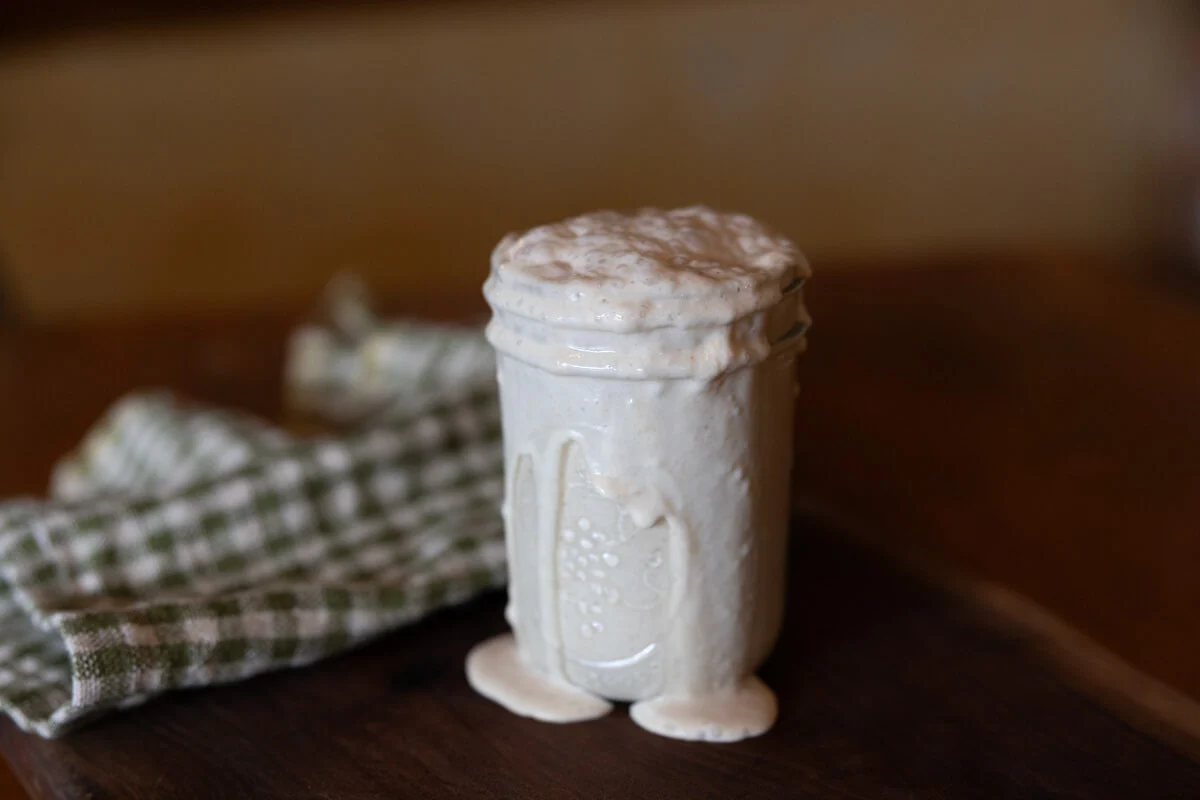 A jar of active sourdough starter at peak rise with visible bubbles along the sides