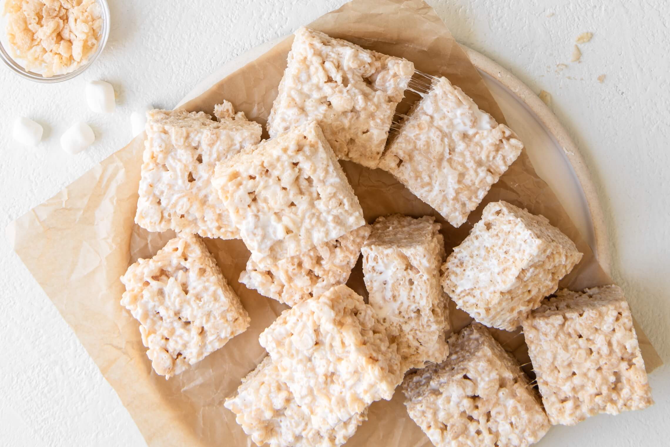 A pan of gooey crisp rice treats with one square lifted to show stretchy marshmallow strands and crisp cereal texture