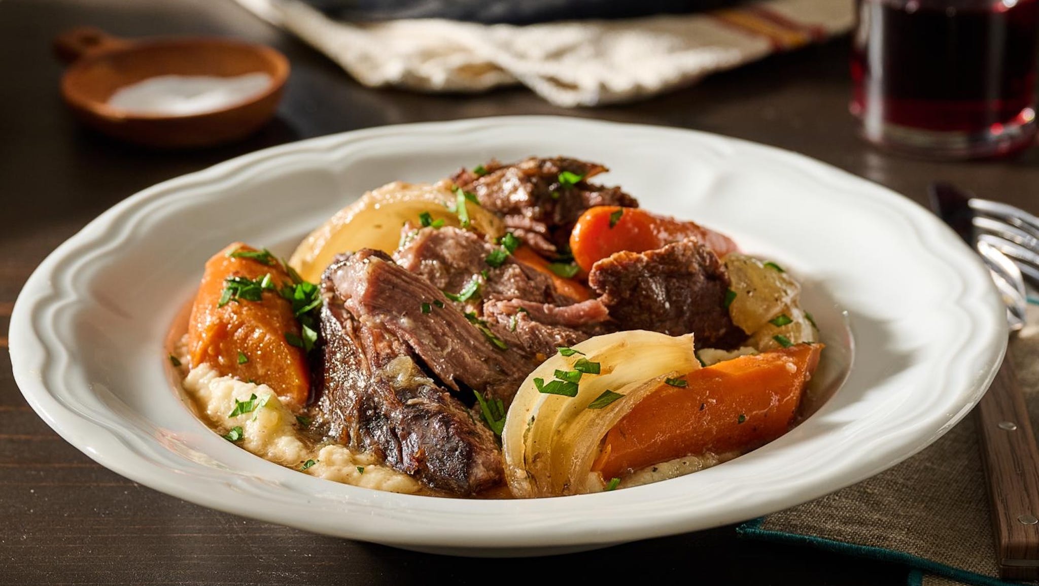 A plated serving of tender crock pot pot roast with carrots and potatoes, spooned with glossy brown gravy on a simple ceramic plate