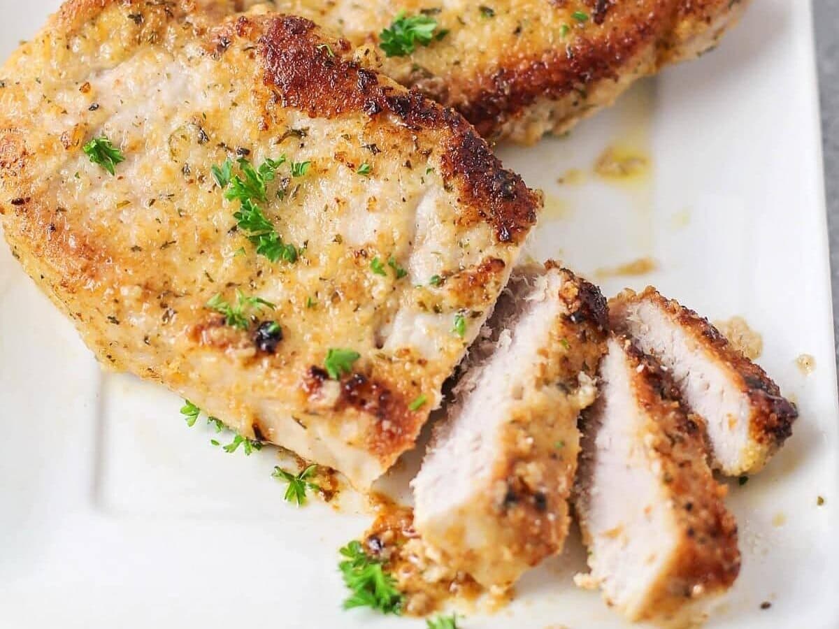 A platter of juicy oven-baked pork chops topped with creamy garlic Parmesan sauce and sprinkled with chopped parsley on a simple dinner table