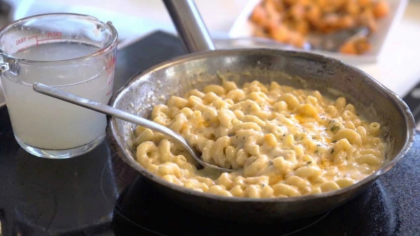 A pot of mac and cheese with a measuring cup of reserved pasta water beside it