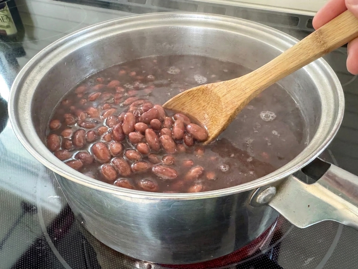A pot of pinto beans gently simmering as a wooden spoon stirs along the bottom