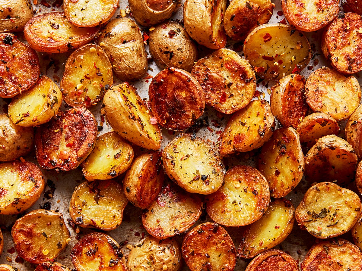 A rimmed sheet pan filled with deeply golden roasted potato chunks with crisp, textured edges and a few sprigs of rosemary scattered around