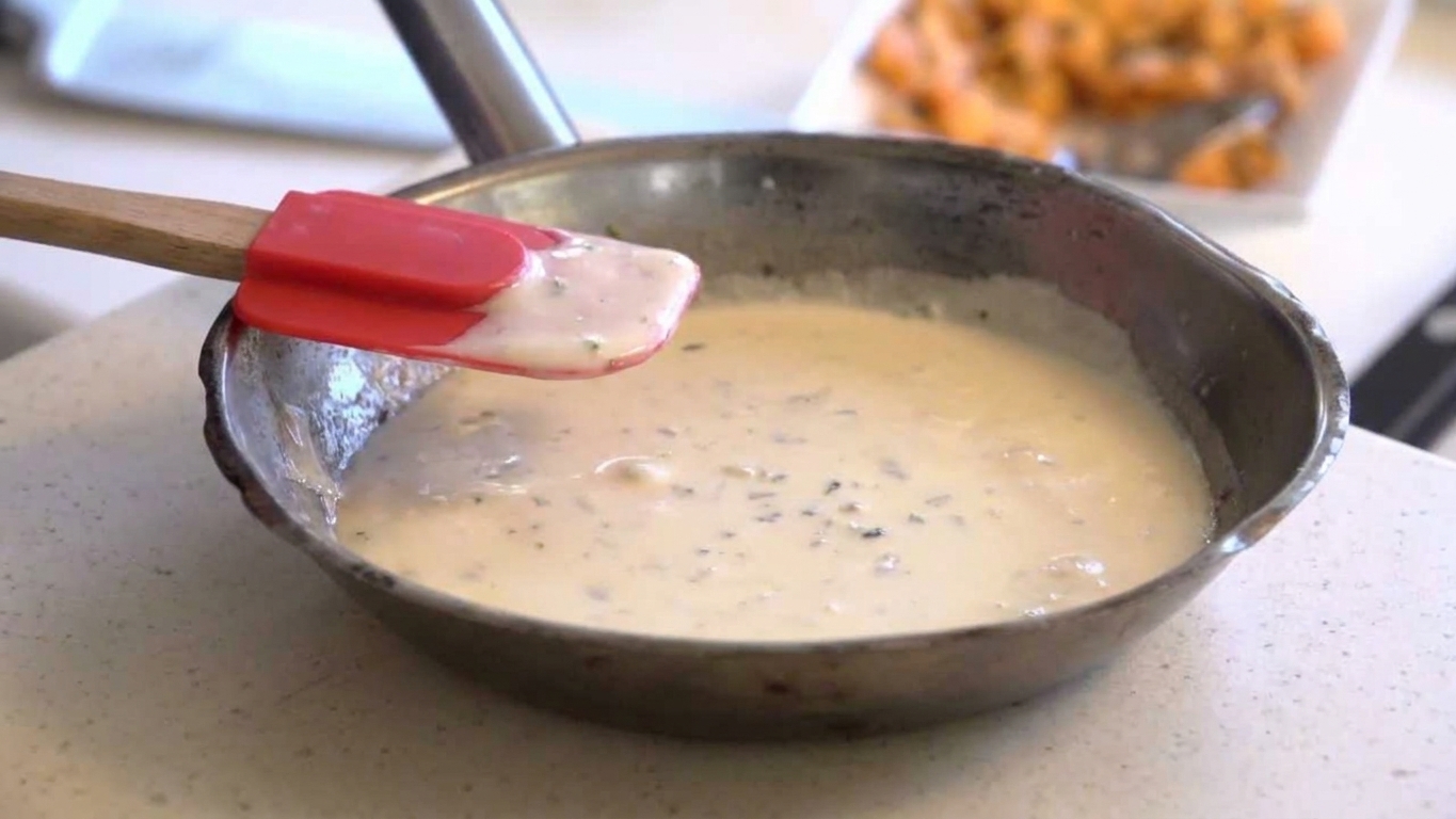 A saucepan of cheese sauce moved off the heat with a silicone spatula resting on the rim