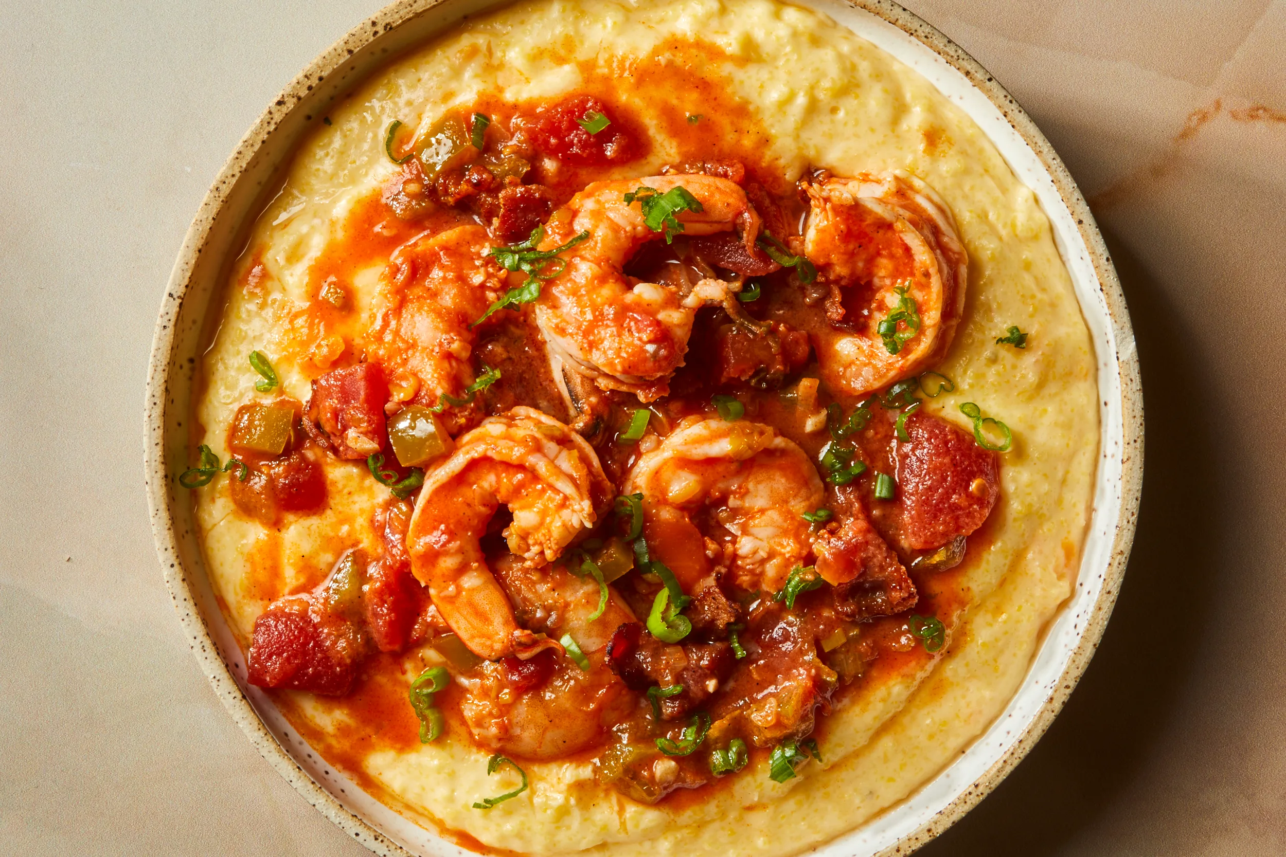 A shallow bowl of creamy grits topped with sautéed seasoned shrimp and a glossy light pan sauce, finished with chopped scallions