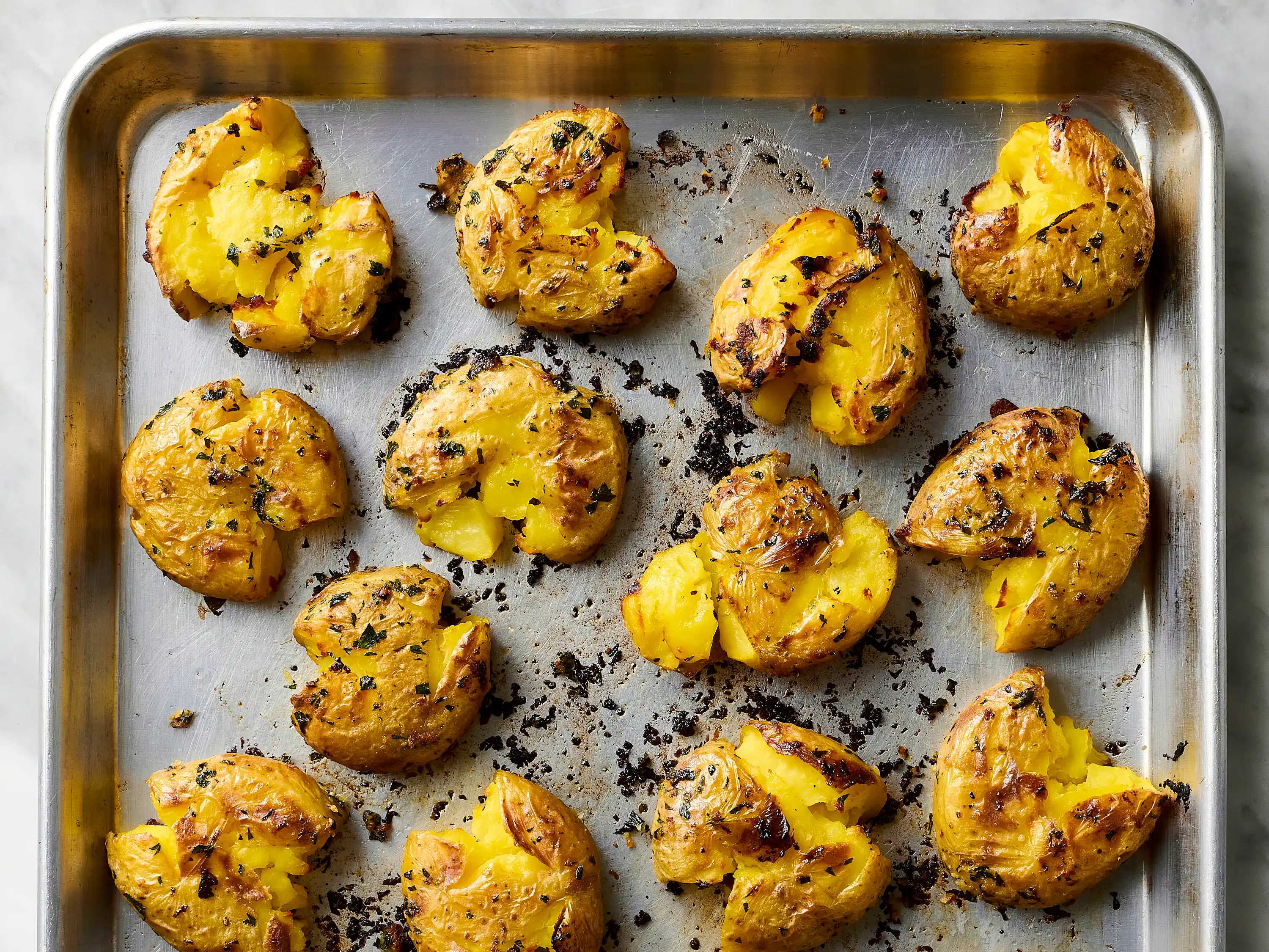 A single oven baked russet potato split open on a plate with crisp, blistered skin and fluffy interior, topped with a small pat of butter