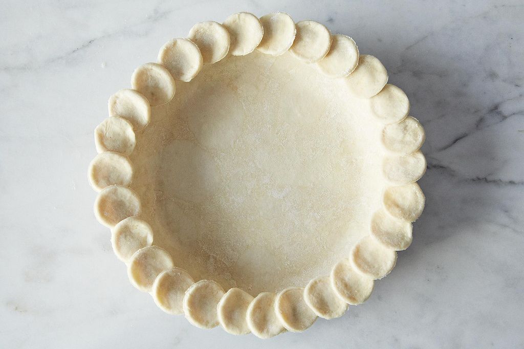 A single unbaked all-butter pie crust rolled into a circle on a lightly floured wooden counter with visible butter flecks
