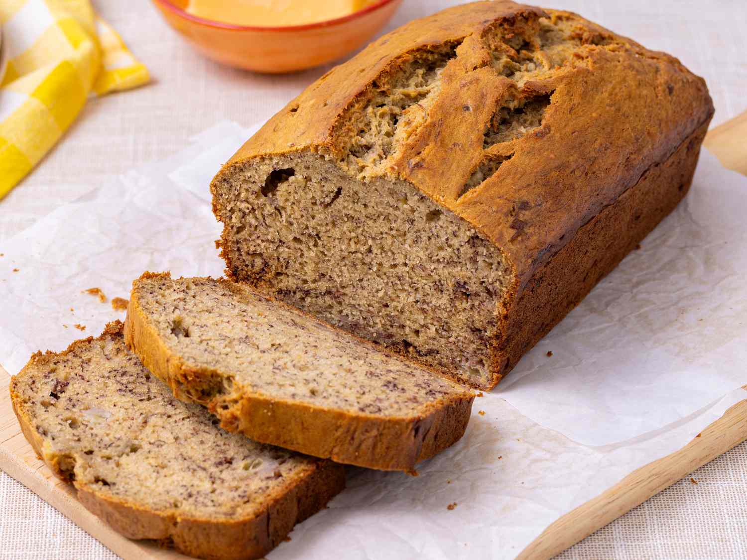 A sliced loaf of classic banana bread on a wooden cutting board with a few crumbs scattered, natural kitchen light