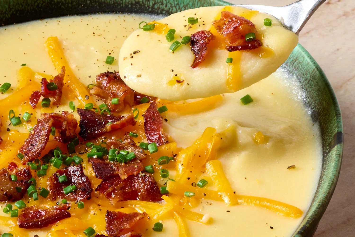 A small wooden board holding toppings for baked potato soup: shredded cheddar, crumbled bacon, sliced scallions, and a dollop of sour cream in a bowl