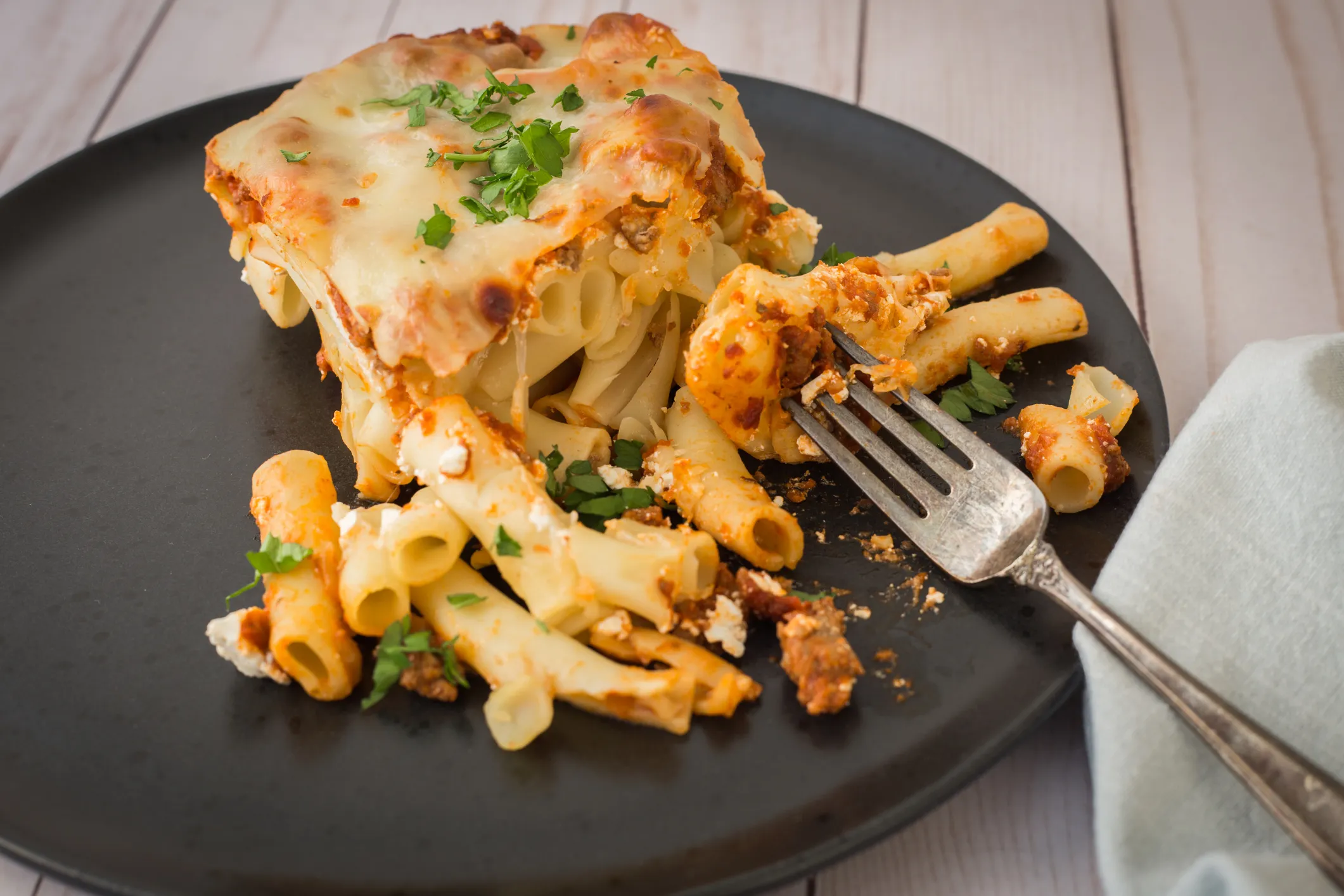 A square slice of tomato pasta bake being lifted from the dish with a spatula, showing stretchy melted cheese