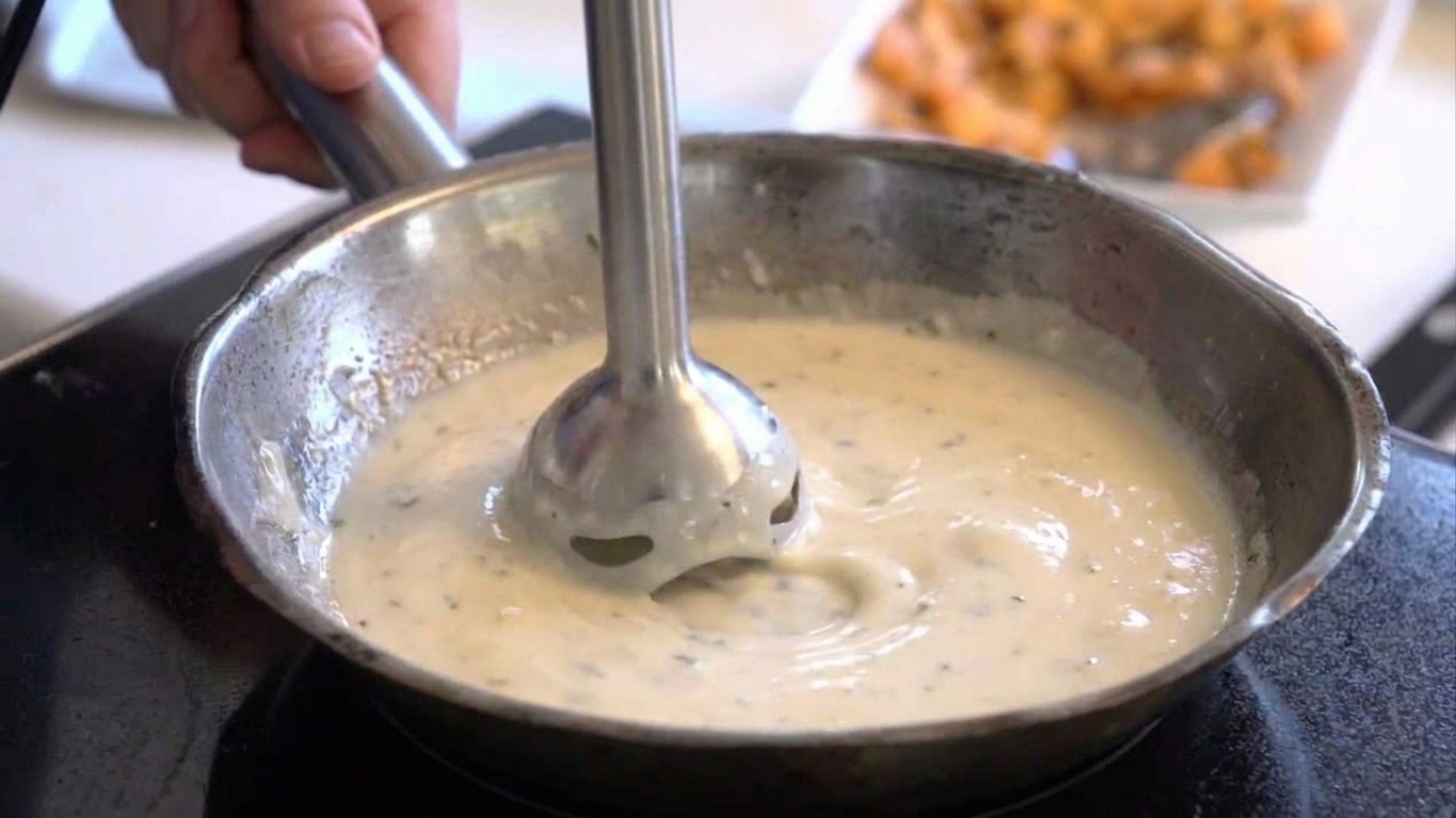 An immersion blender smoothing a pot of cheese sauce until it becomes glossy