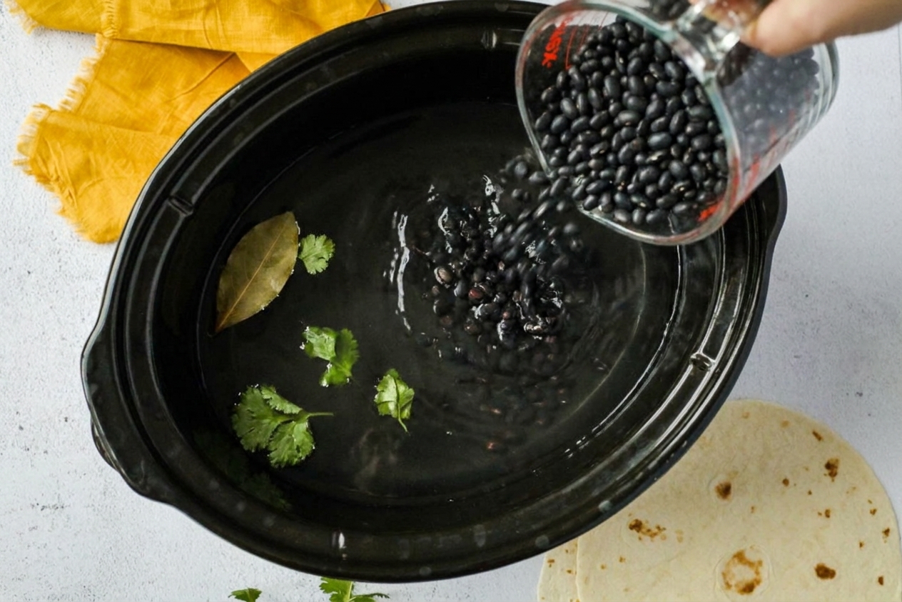 Dry black beans being poured into a slow cooker insert with water already inside
