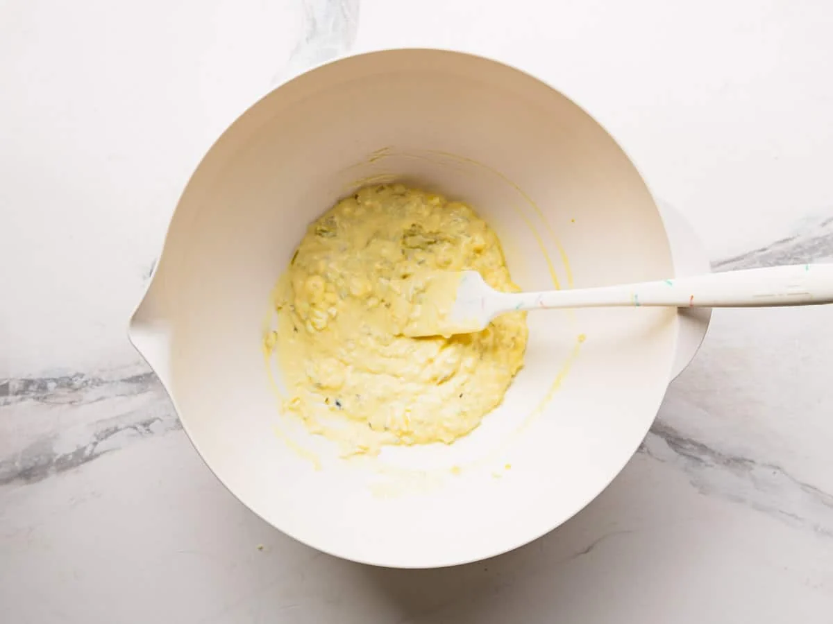 Hands gently folding warm potatoes with creamy dressing in a large bowl using a rubber spatula