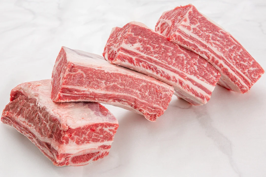 Raw bone-in beef short ribs on a butcher paper lined tray
