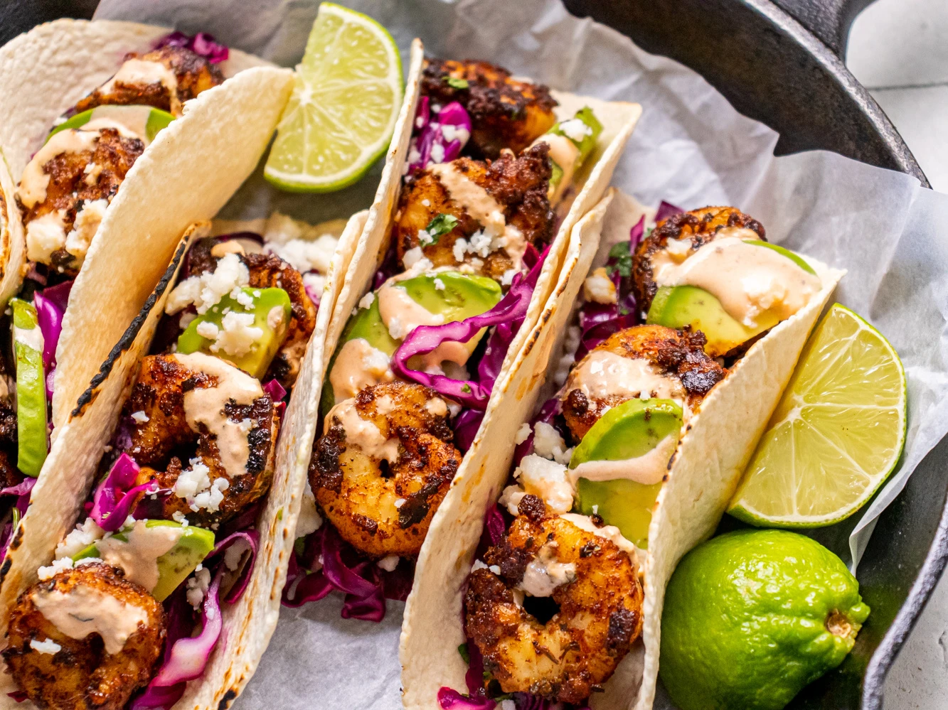 Shrimp, shredded cabbage, limes, cilantro, yogurt, and spices arranged on a kitchen counter ready for tacos