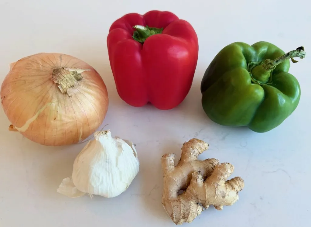 Sliced onions, chopped bell peppers, and minced garlic on a cutting board with a chef's knife