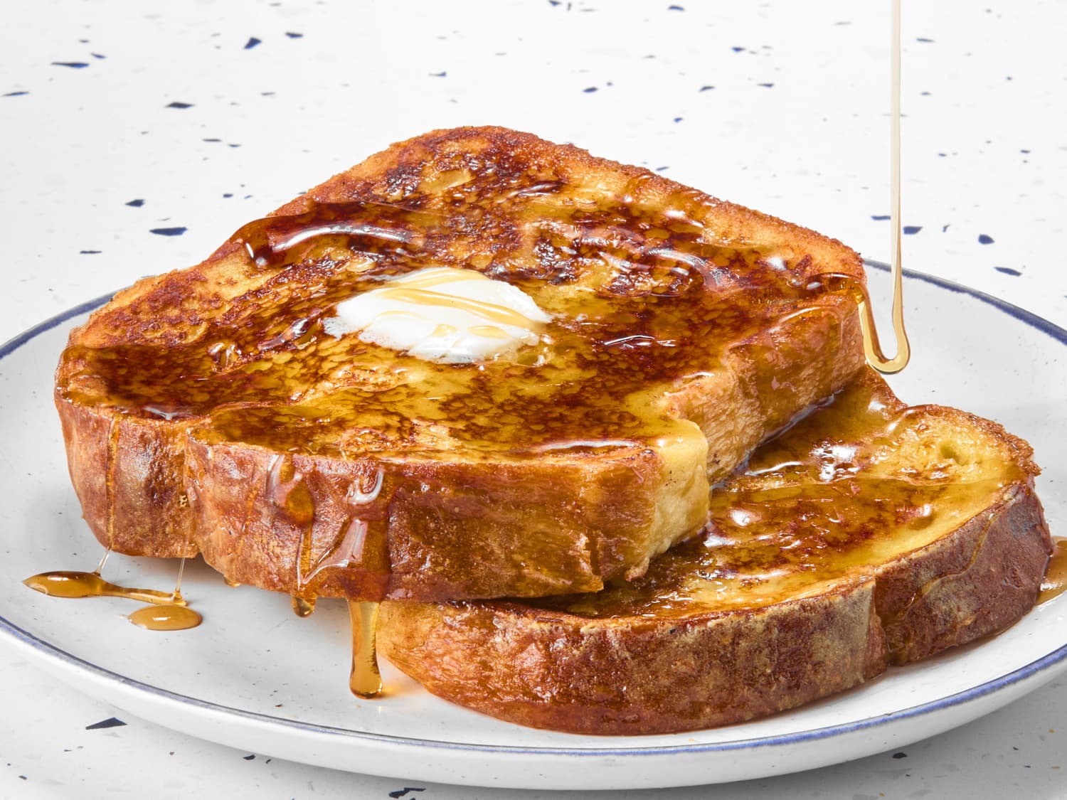 Two thick slices of golden brown French toast on a ceramic plate with a pat of butter melting on top and a light dusting of powdered sugar